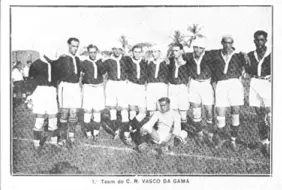 Time de futebol em preto e branco, uniformes pretos e brancos, árvore e céu claro ao fundo.