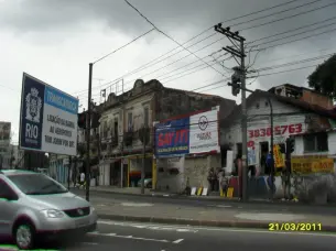 Rua em Madureira, Rio de Janeiro, com carro cinza, prédios coloridos e sinal de trânsito.