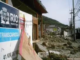 Área destruída após desastre natural, cartaz da Prefeitura do Rio visível.