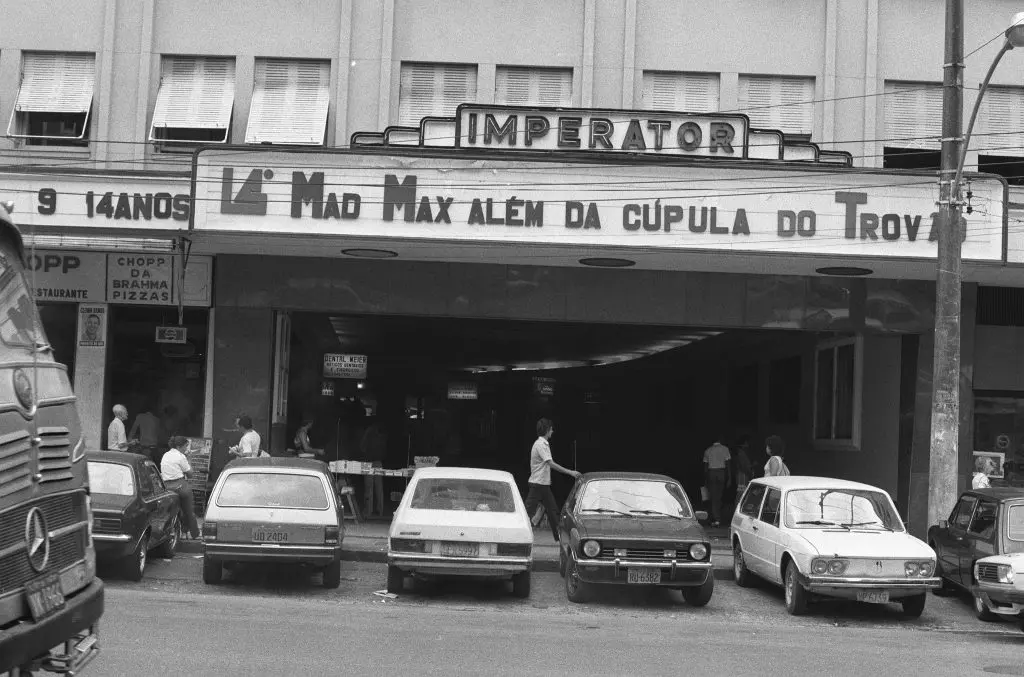 Cinema localizado em subúrbio com letreiro "IMPERATOR" e anúncios de filmes e chopp.