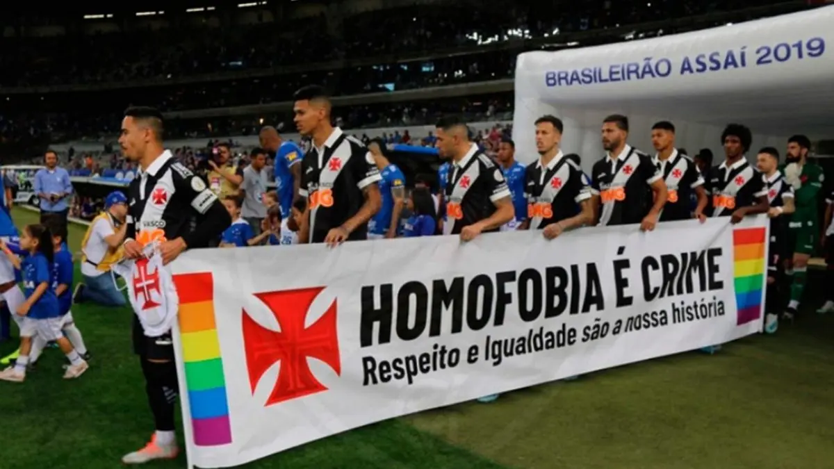 Jogadores uniformizados em preto e branco segurando faixa contra homofobia.