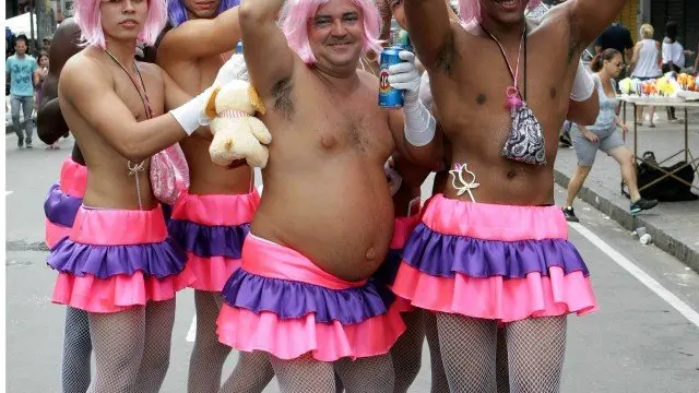 Três mulheres em miniskirts coloridos, sorridentes, com garrafa de refrigerante, evento festivo.