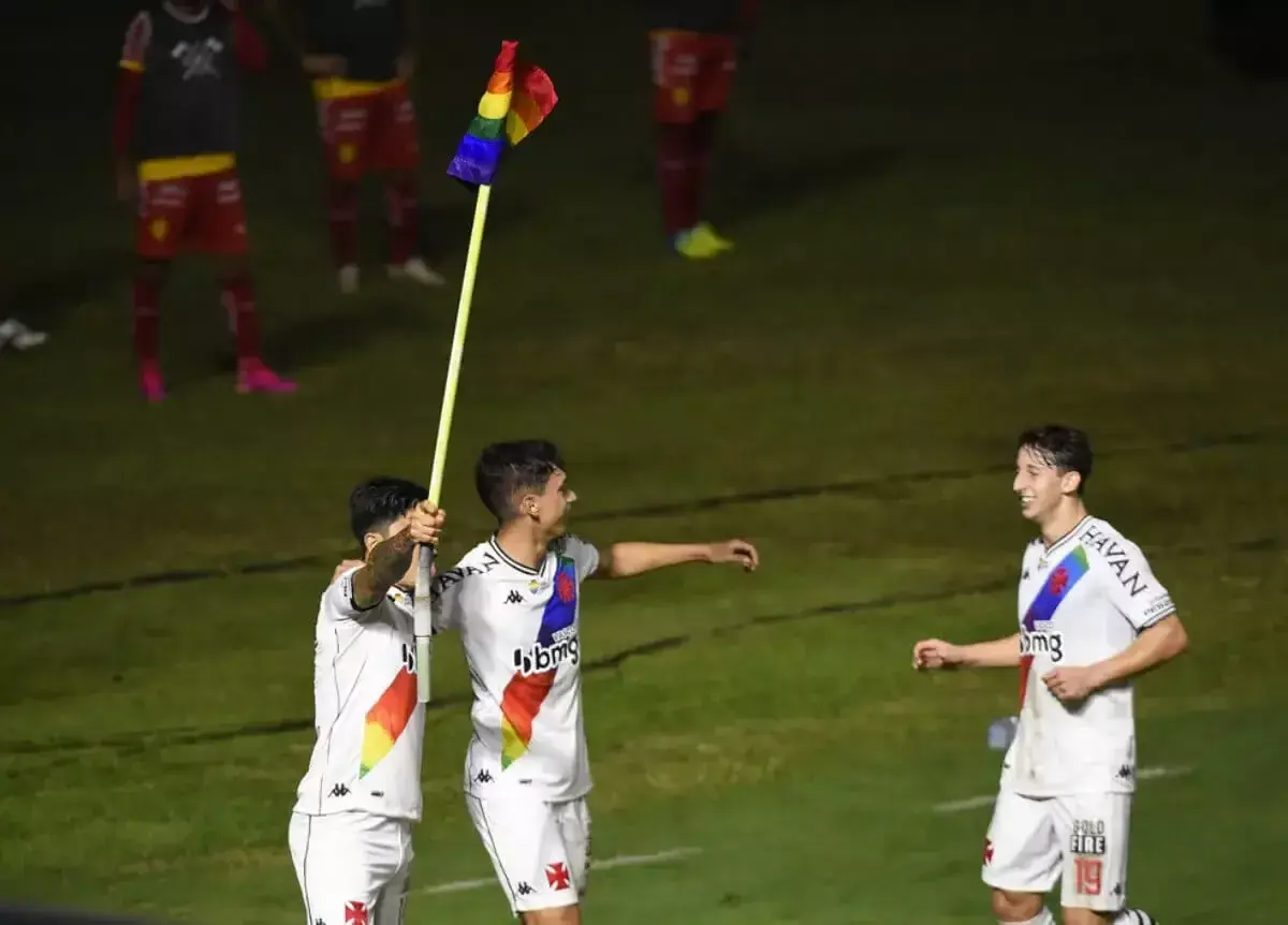 Três jogadores de futebol em campo à noite, uniformes brancos e vermelhos.