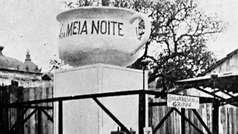 Objeto xícara "A MEIA NOITE", concreto, árvore sem folhas, prédios antigos, placa "CONCURRÊNCIA GRIPPE".