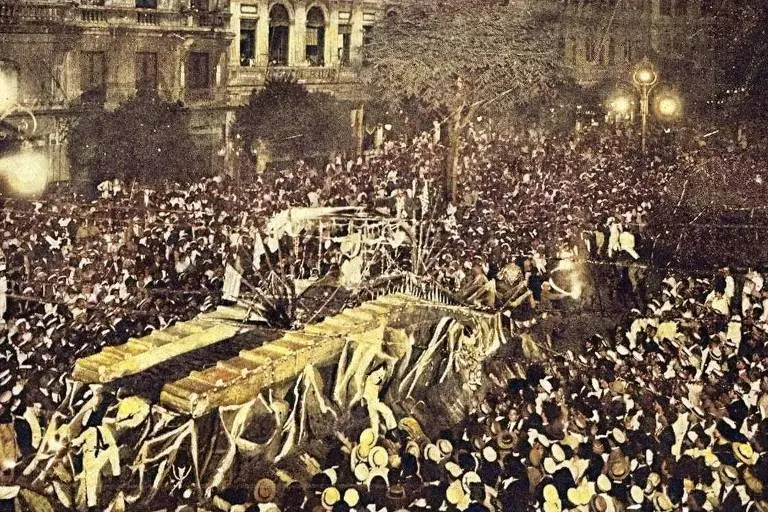 Multidão密集拥挤 em evento público, possível funeral, com cortejo funerário e caixão coberto por bandeira branca.