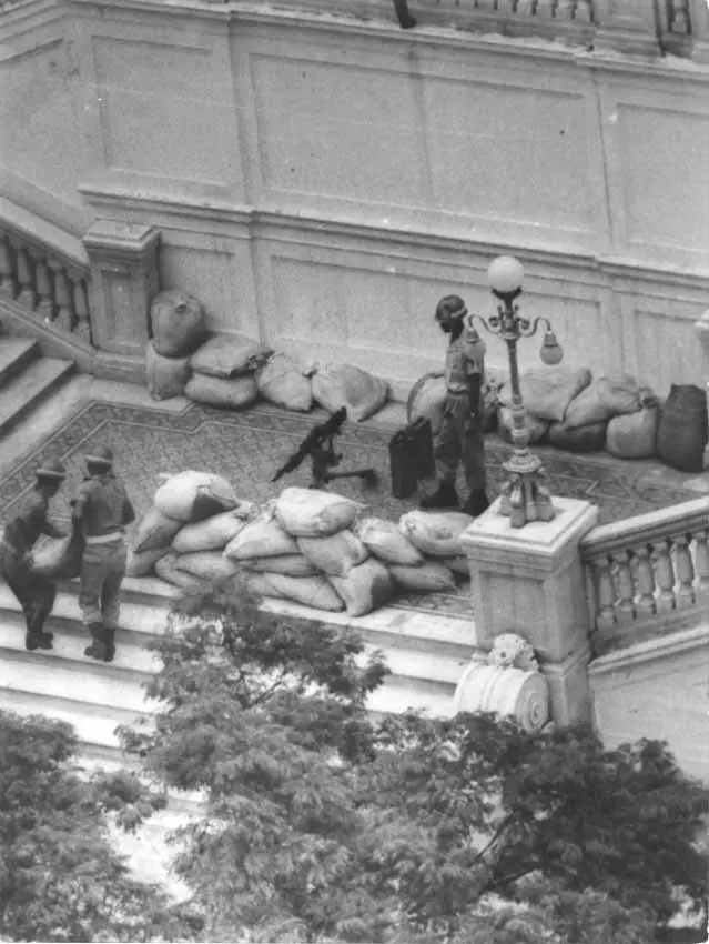 Grupo de pessoas carregando sacos de areia em frente a edifício com escadaria.