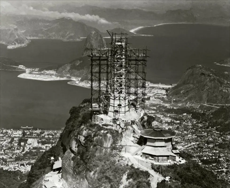 Paisagem montanhosa com monumento em construção e cidades ao longo da costa.