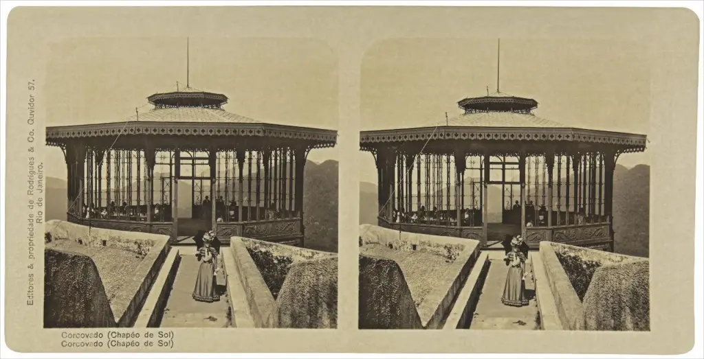 Cartão-postal preto e branco mostrando arquitetura com telhado abobadado e cobertura metálica, com vista para montanhas e duas pessoas históricas.