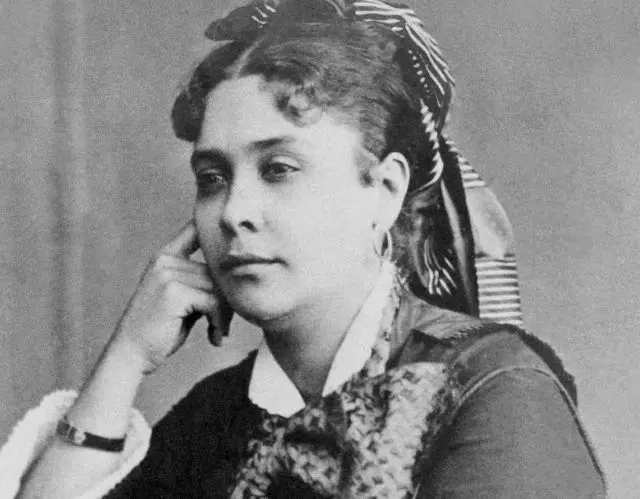 Mulher sentada, rosto para esquerda, penteado elaborado, vestido floral, fundo neutro.