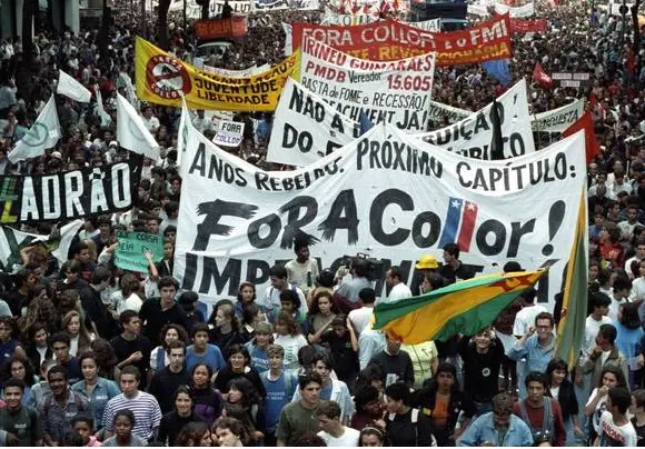 Manifestação pública com faixas e bandeiras amarelas em um ambiente urbano.