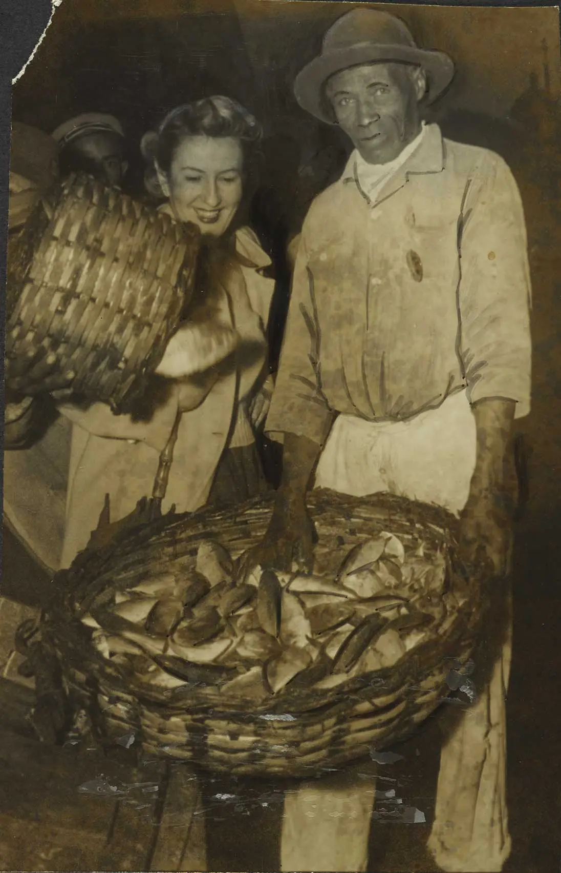 Três pessoas em mercado antigo com cestas de peixes.