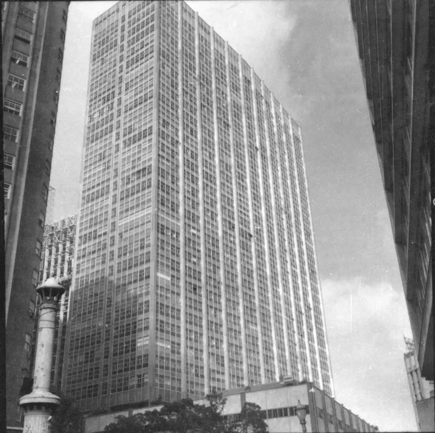 Edifício moderno com arranha-céu e estruturas ao fundo.