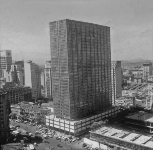 Edifício moderno em área urbana com arranha-céu e paisagem urbana ao fundo.