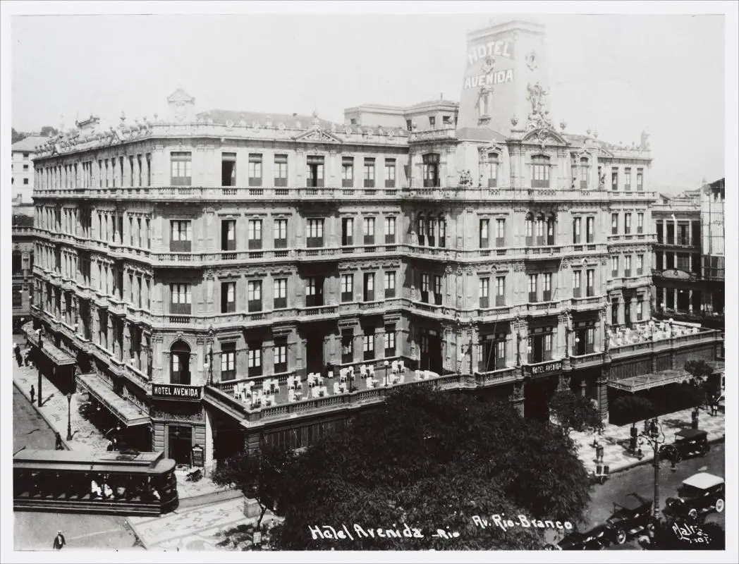 Edifício "Hotel Avenida" em preto e branco, com plataforma elevada e árvores à frente.