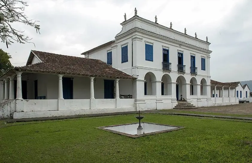 Edifício principal de fazenda histórica com ala à esquerda e poço no centro.