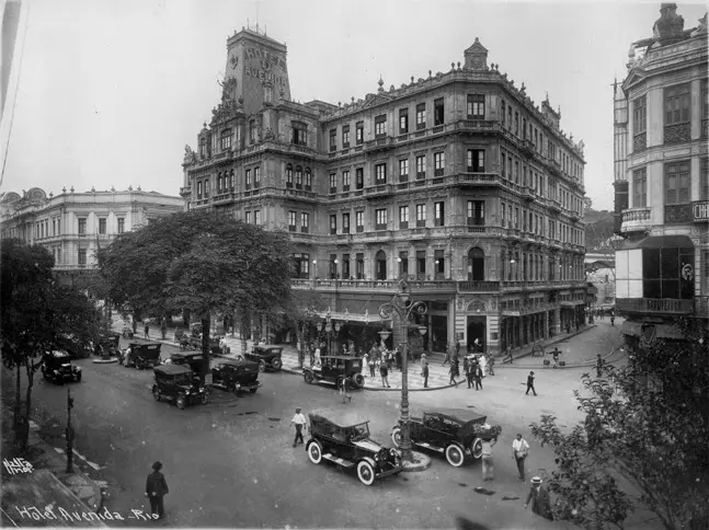Hotel clássico em avenida com praça e edifícios ornamentados.