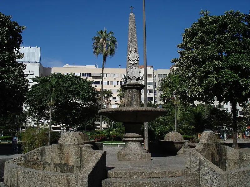 Espaço público com fonte central e vasos de pedra.