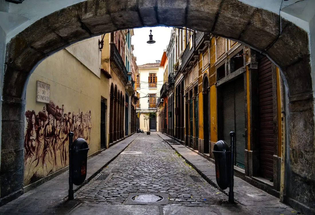 RUA ESTREITA COM ARCO DE PEDRA E PAREDE AMARELA.