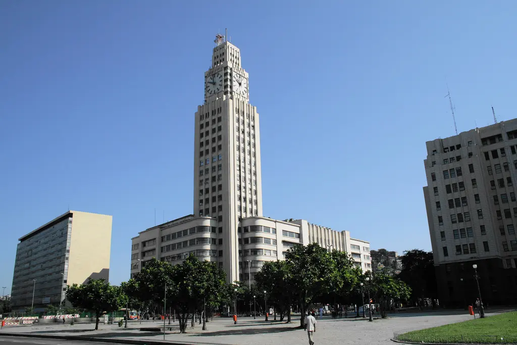Edifício com torre e prédios adjacentes em espaço público.