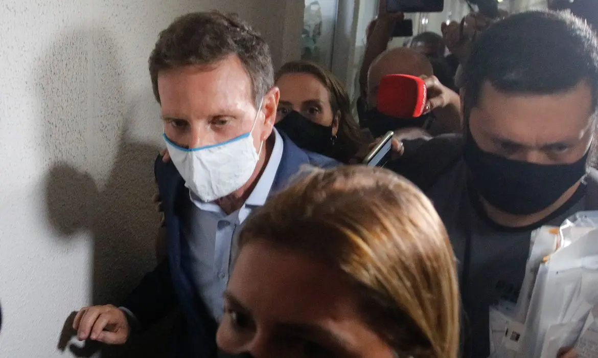 Grupo de pessoas em corredor, com textura branca à esquerda e máscaras e objetos brancos.