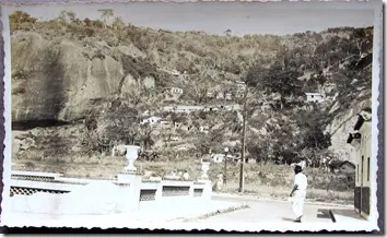 Casa à esquerda, homem caminhando, paisagem com rocha e colina.