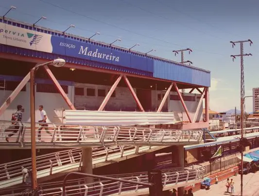 Estação Madureira com telhado azul e branco, logotipo da Supervia e pessoas caminhando.