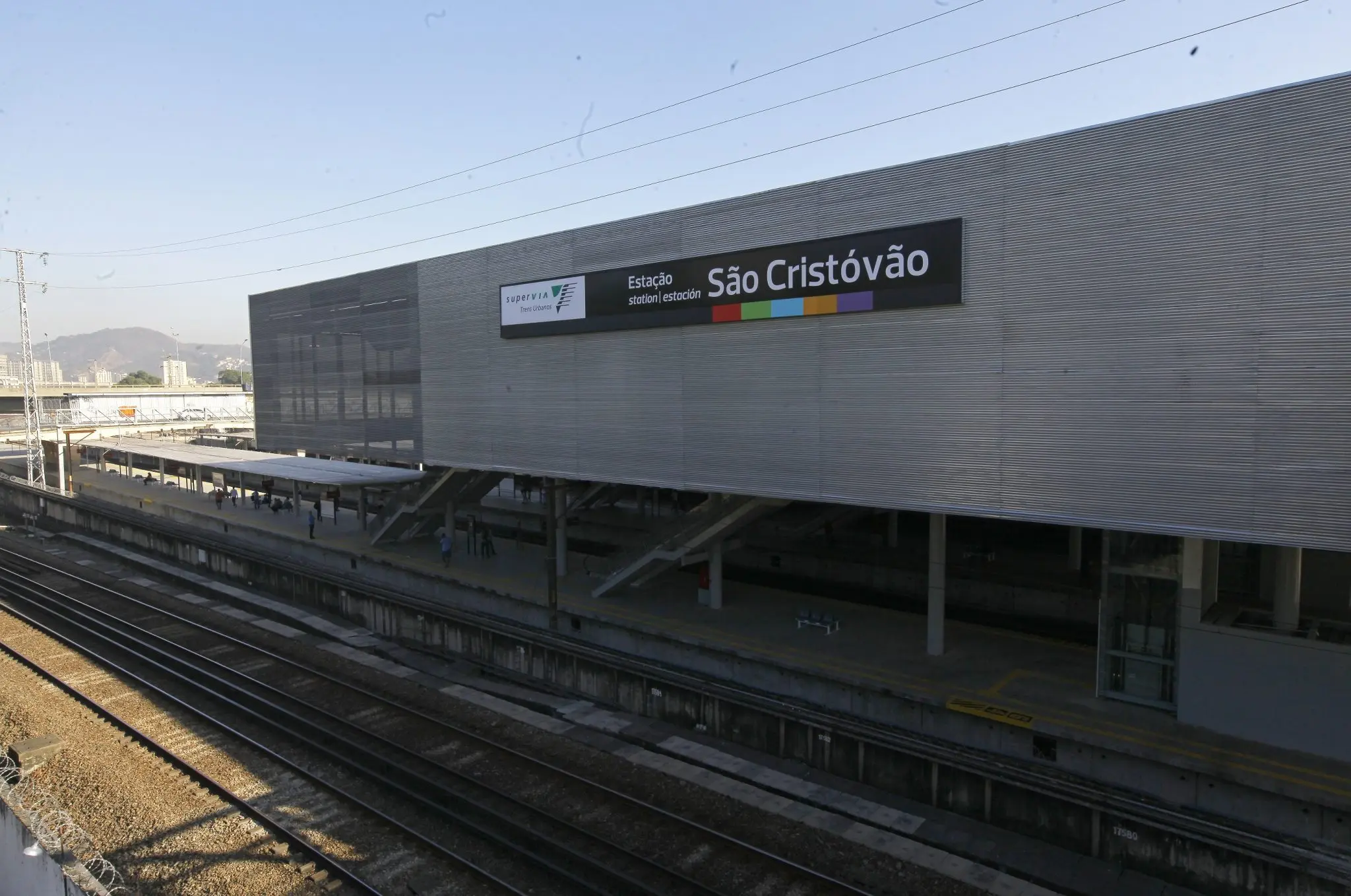 Estação ferroviária moderna com plataforma e edifício cinza metálico.