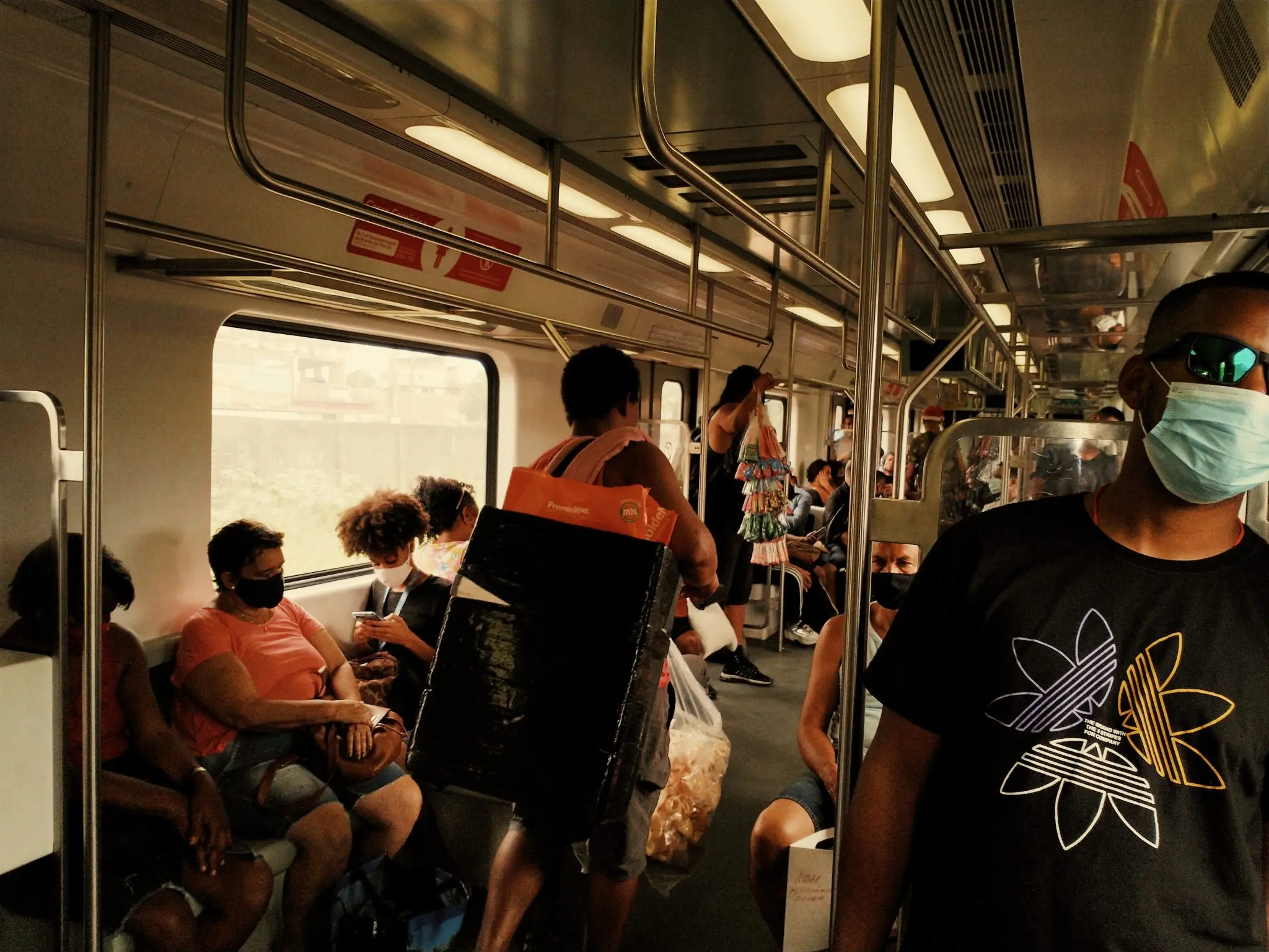 Trem lotado com pessoas sentadas e de pé, iluminação quente.