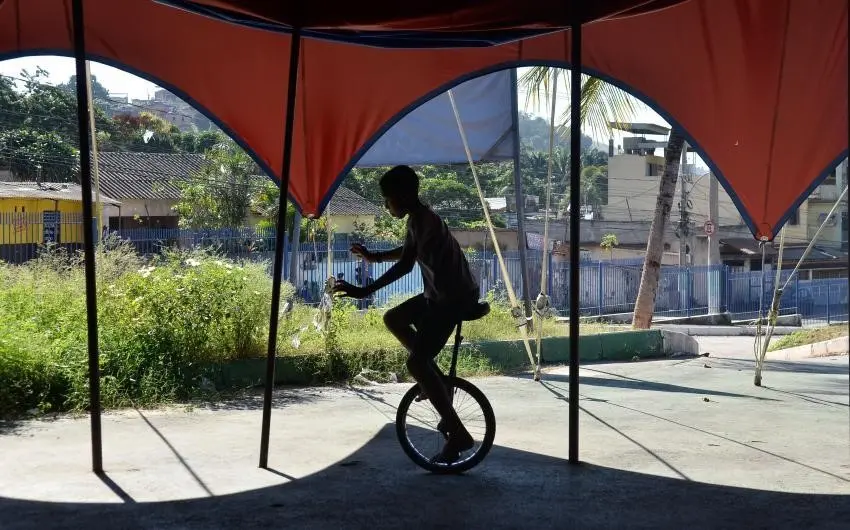 Homem equilibra monocicleta sob tenda vermelha.