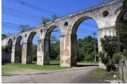 Aqueduto antigo com arcos de pedra em terreno verde.