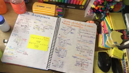 Caderno com anotações coloridas e suprimentos escolares.
