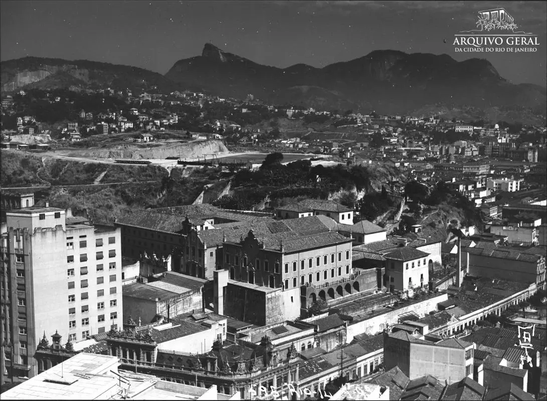 Cidade com montanhas ao fundo, edifícios e logotipo da Arquivo Geral da Cidade do Rio de Janeiro.