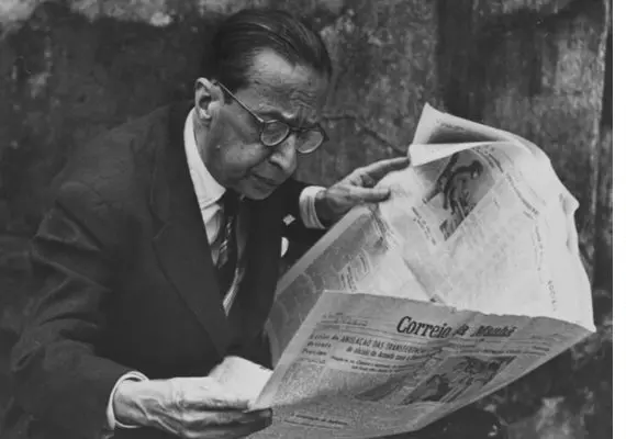 Uma pessoa lendo jornal em preto e branco.