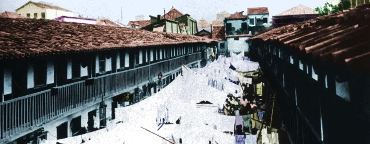 Uma rua estreita com construções antigas, lençóis pendurados e telhados de telha vermelha.