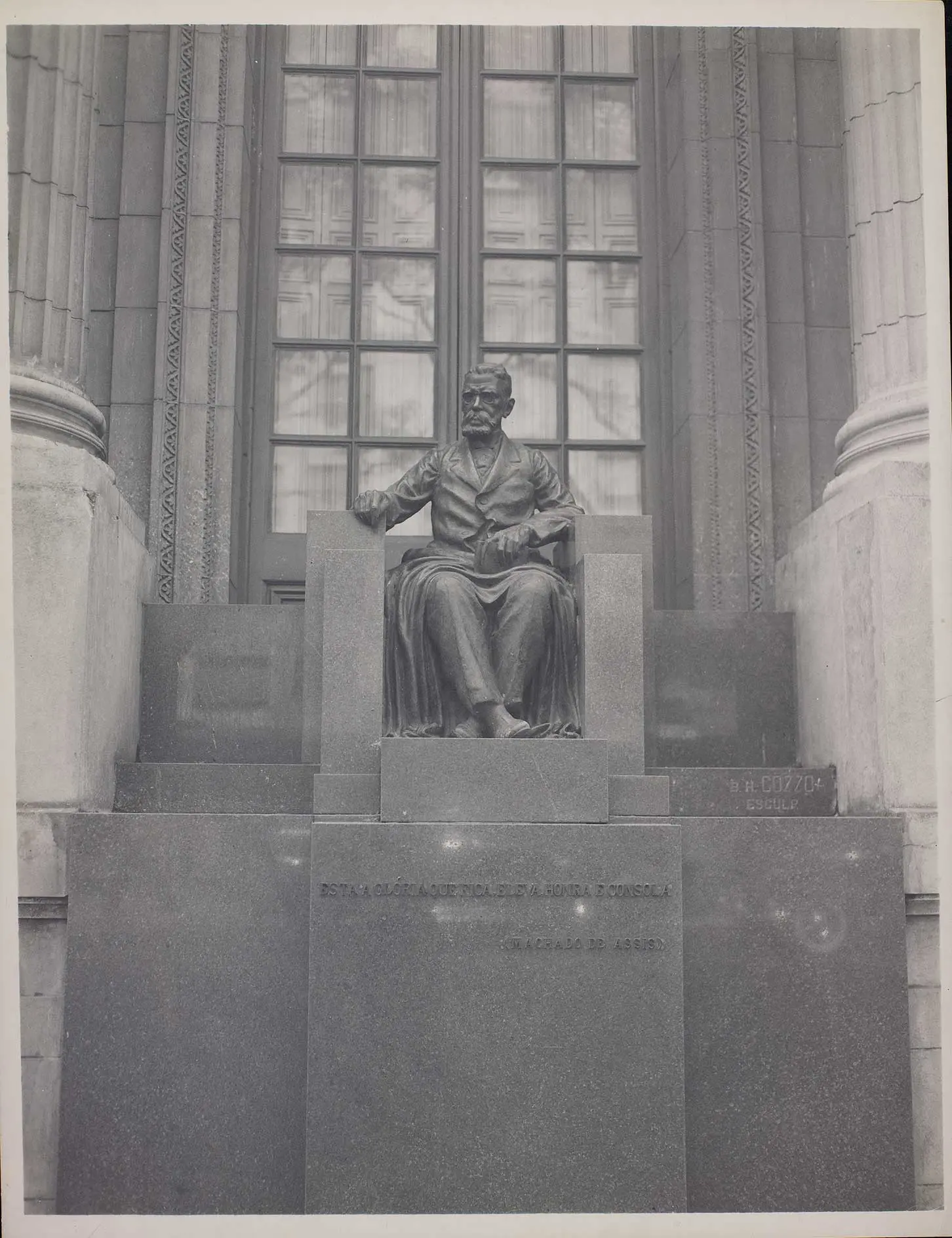 Estátua em trono em frente a edifício clássico com vitrais.