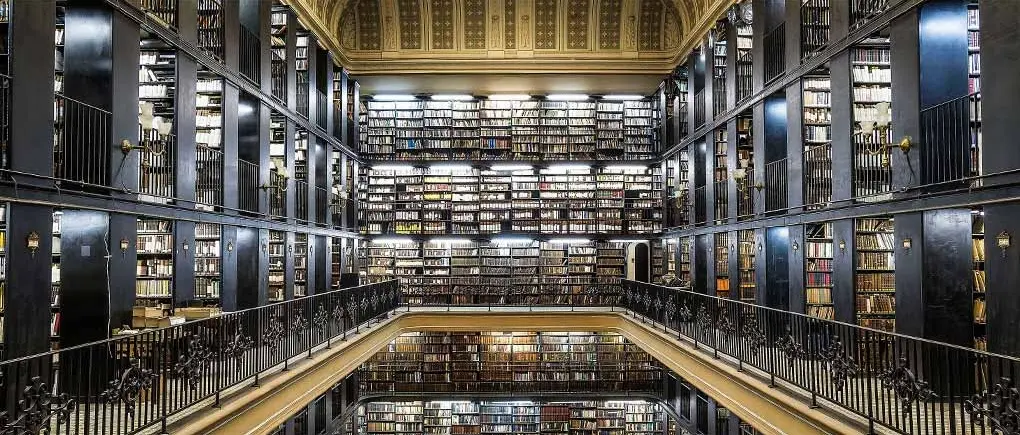 Biblioteca histórica com prateleiras altas e iluminação natural.