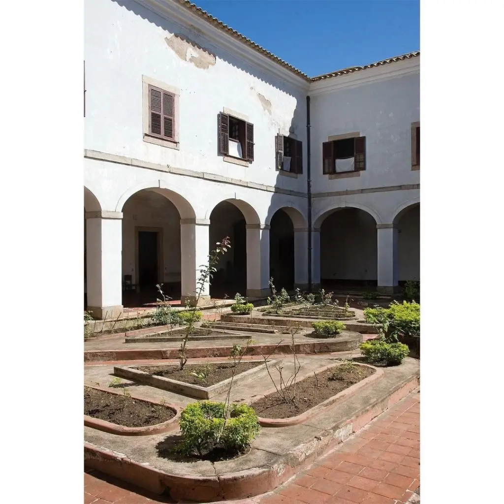Pátio interno de convento com jardins e telhado vermelho.