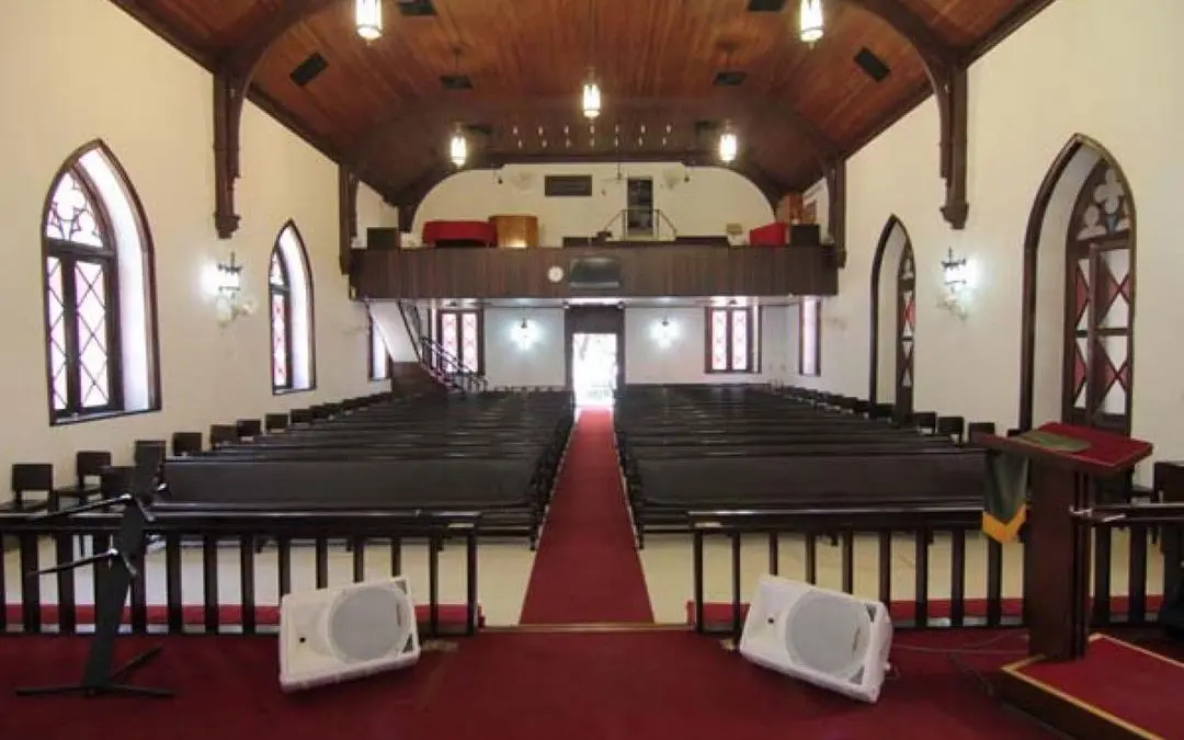 Interior de igreja com bancos, vitrais coloridos e corredor vermelho.