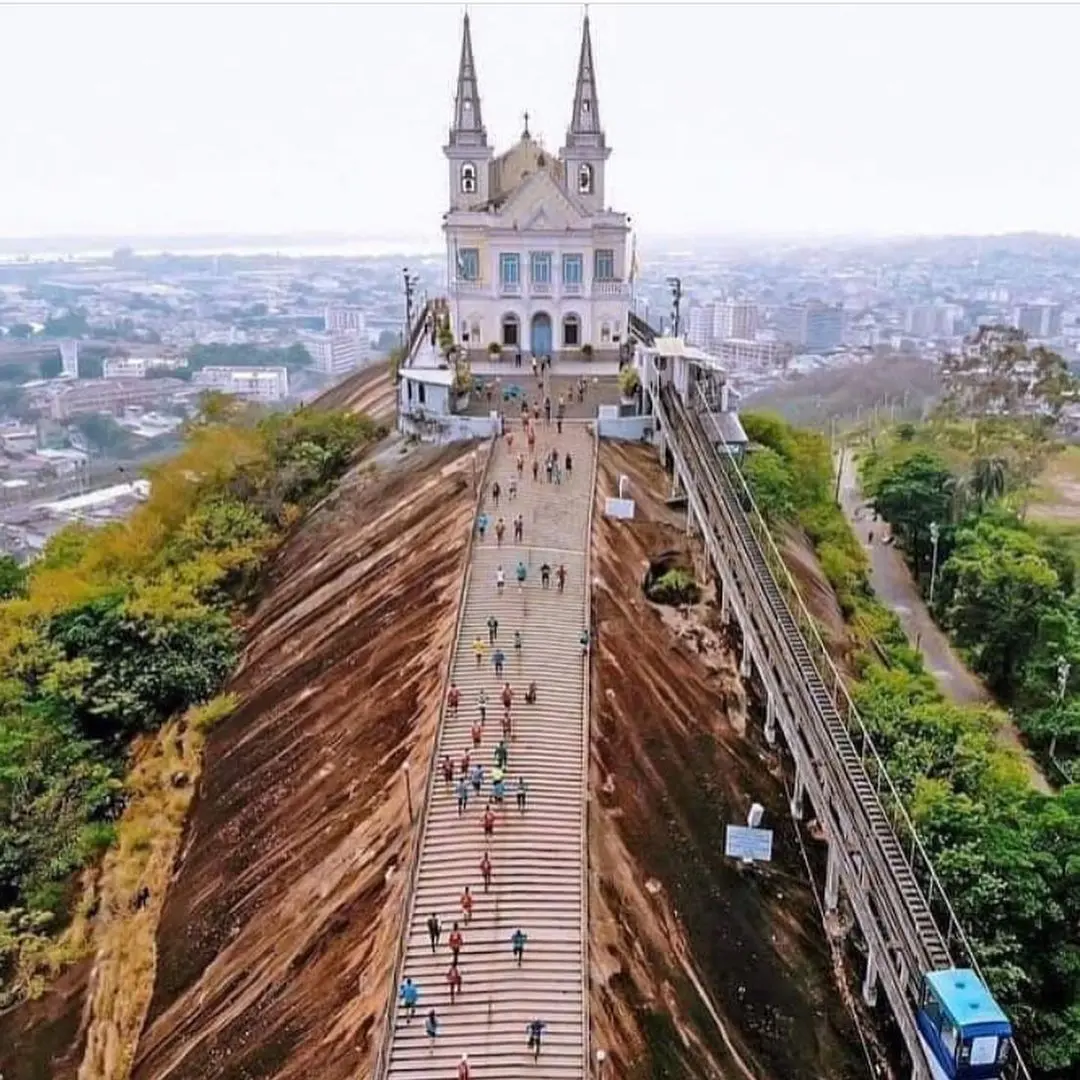 Igreja em penhasco com torres altas e teleférico azul.