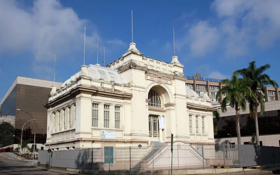 Edifício neoclássico em ambiente urbano com palmeiras e prédios modernos.