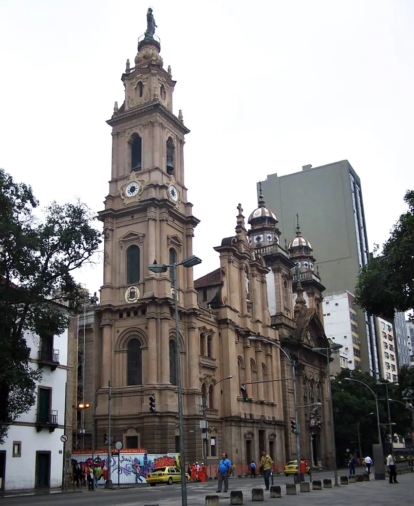 Igreja histórica em São Paulo com torre e relógio, edifícios modernos e arquitetura contrastante.