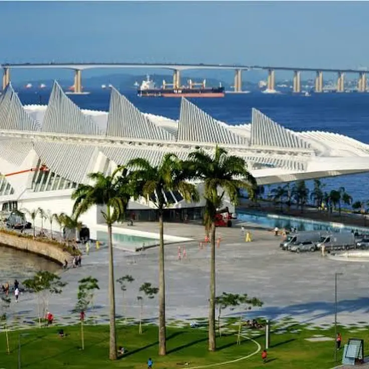 Edifício moderno com palmeiras e ponte sobre o mar.