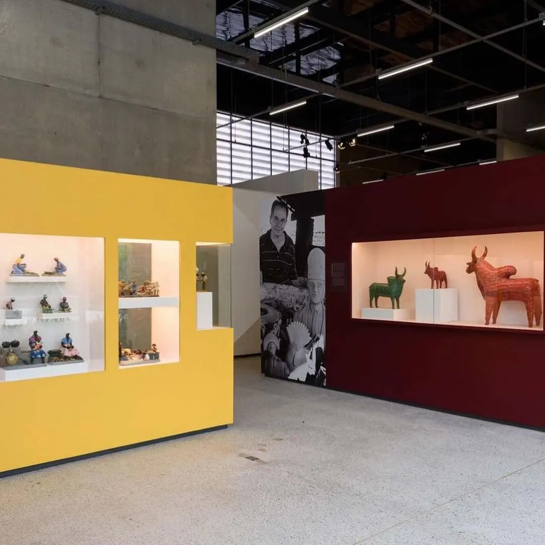 Exposição em museu com objetos pequenos e detalhados à esquerda, esculturas de animais à direita e foto preto e branco no centro.