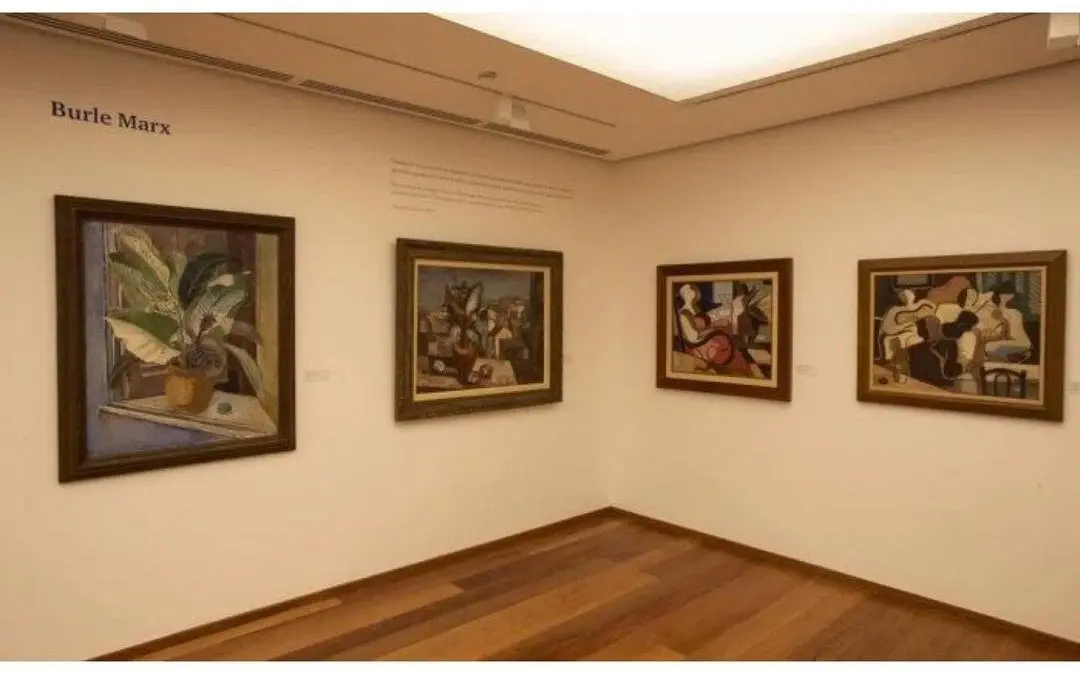 Galeria de arte com quadros de plantas e figuras humanas em tons de azul, verde e vermelho.