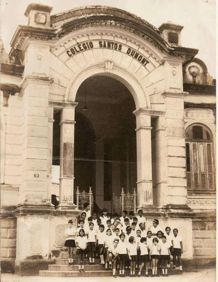 Colégio Santos Dumont em preto e branco, entrada com arco e crianças em uniforme.