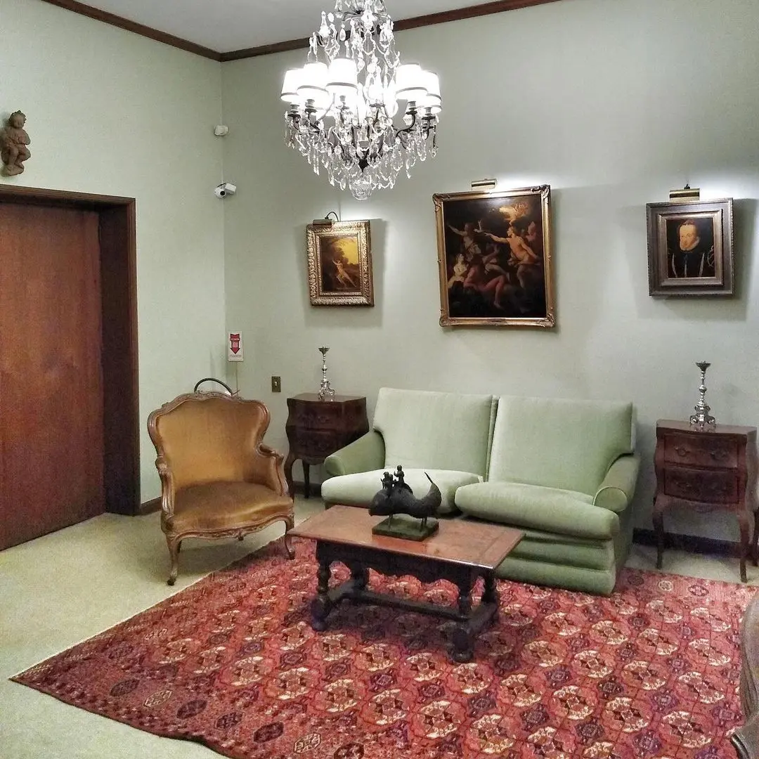 Interior clássico com sofá verde, mesa de centro e quadros.