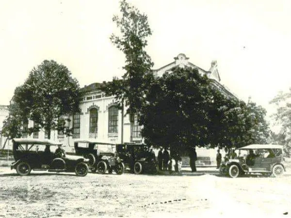 Edifício clássico com árvores e carros antigos em preto e branco.