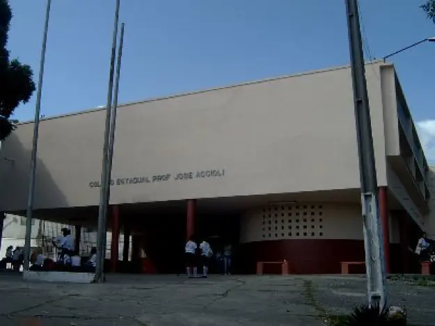Prédio escolar com árvore e pessoas caminhando.