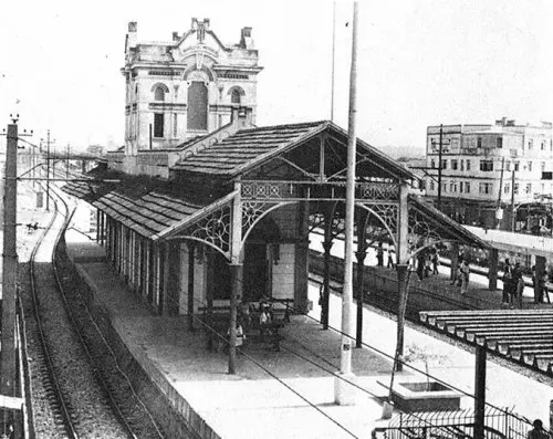 Estação ferroviária antiga com trilhos e cobertura metálica.