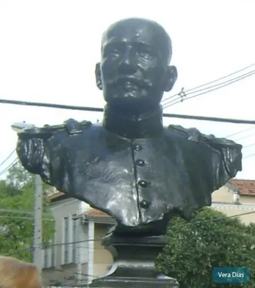 Estátua de bronze de militar em frente à casa vermelha.